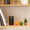IGELBALL SET Verpackung und zwei Igelbälle, ein grüner und ein orangefarbener, auf einem Regal neben Büchern und Pflanzen.
