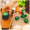 Hand hält einen grünen Massageball, daneben ein grüner Triggerpunkt Drücker auf einem Holztisch.